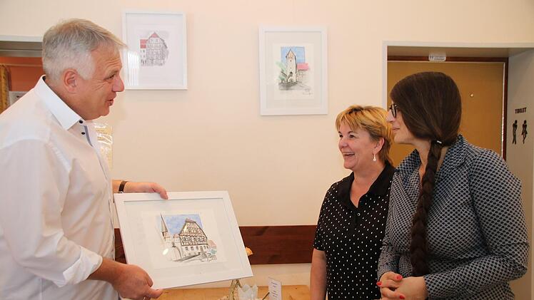 Thomas Geyer zeigt Susanne Hanshans (Mitte) und Susanne Stäblein (rechts)  das Aquarell vom Heimatspielhaus. Dieses und 22 andere sollen zugunsten des Vereins verkauft werden.Thomas Malz