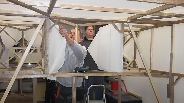 Die Konstruktion aus Holzlatten ist so groß, dass man dazwischen "herumlaufen" kann. Hier tackert Roland Klinger Stoff an die Latten. Hinten Markus Merkl