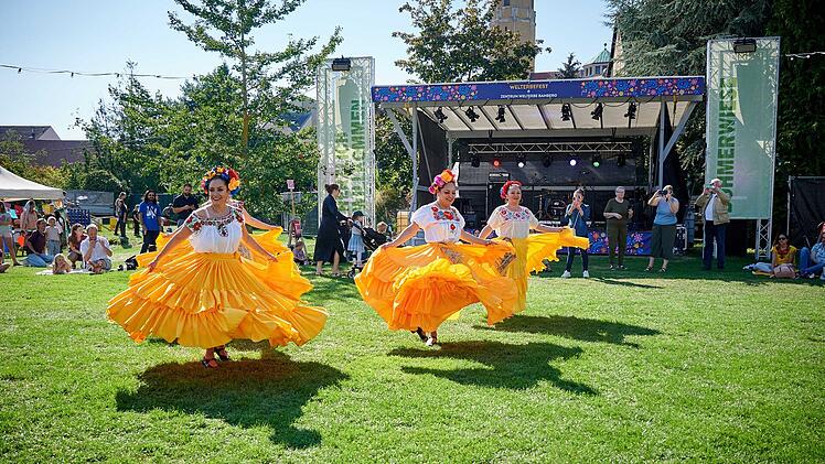 Mexikanische Tänzerinnen in bunten, gelben Kleidern performen beim Welterbefest in Bamberg. Im Hintergrund sitzen Zuschauer und eine Bühne ist zu sehen.