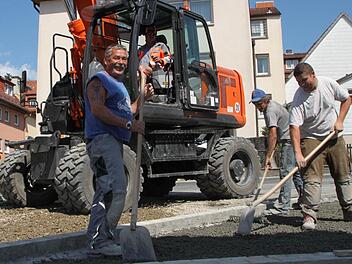 Bei 22 Grad im Schatten bringen Klaus Kürschler, Dominik Sands und Simon Fischer Drain-Beton auf die Fahrbahn auf. Baggerfahrer Edwin Kolb überblickt die Arbeiten vom Führerhaus aus. Foto: Ulrike Müller