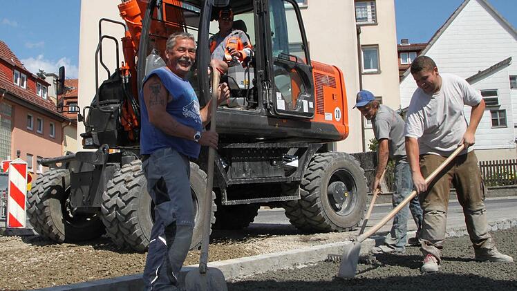 Bei 22 Grad im Schatten bringen Klaus Kürschler, Dominik Sands und Simon Fischer Drain-Beton auf die Fahrbahn auf. Baggerfahrer Edwin Kolb überblickt die Arbeiten vom Führerhaus aus. Foto: Ulrike Müller