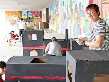 Die Lokomotiven aus Riesenkartons sind fertig. Mit dem Farbpinsel bringen Diana Held (rechts) und ihre Schüler auf unserem vor wenigen Tagen entstandenen Bild noch Details wie Räder oder Lichter an. Foto: Popp