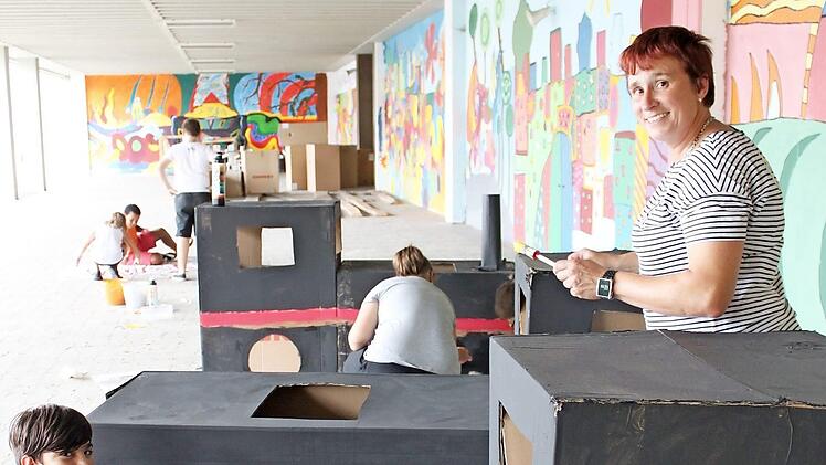 Die Lokomotiven aus Riesenkartons sind fertig. Mit dem Farbpinsel bringen Diana Held (rechts) und ihre Schüler auf unserem vor wenigen Tagen entstandenen Bild noch Details wie Räder oder Lichter an. Foto: Popp