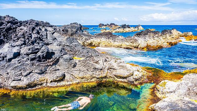 Unbekannter Mann beim Schnorcheln in natürlichen Schwimmbecken an der felsigen Küste der Stadt Mosteiros auf der Insel São Miguel, Azoren, Portugal. Unidentified man snorkelling in natural swimming pools on rocky coast in Mosteiros town, Sao Miguel island, Azores, Portugal