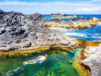Unbekannter Mann beim Schnorcheln in natürlichen Schwimmbecken an der felsigen Küste der Stadt Mosteiros auf der Insel São Miguel, Azoren, Portugal. Unidentified man snorkelling in natural swimming pools on rocky coast in Mosteiros town, Sao Miguel island, Azores, Portugal