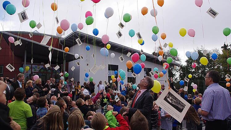 Kinder und Erwachsene lassen vor der Schule Luftballons steigen.