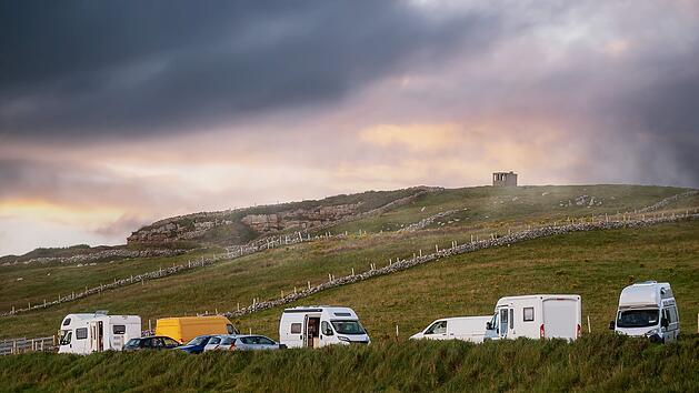 Parkplatz mit Wohnmobilen und Wohnwagen auf einer gr&uuml;nen Wiese bei Sonnenuntergang. Warmer und k&uuml;hler Ton. Reise- und Tourismuskonzept. Grafschaft Sligo, Irland. Tourist camping in einem sch&ouml;nen Land Seite.  Car park with motor home and camper vans by a green field at sunset. Warm and cool tone. Travel and tourism concept. County Sligo, Ireland. Tourist camping in a beautiful country side.