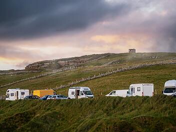 Parkplatz mit Wohnmobilen und Wohnwagen auf einer grünen Wiese bei Sonnenuntergang. Warmer und kühler Ton. Reise- und Tourismuskonzept. Grafschaft Sligo, Irland. Tourist camping in einem schönen Land Seite.  Car park with motor home and camper vans by a green field at sunset. Warm and cool tone. Travel and tourism concept. County Sligo, Ireland. Tourist camping in a beautiful country side.