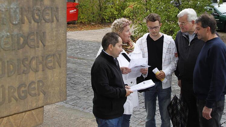 Atilla Karabag, Marita Obermeyer-Simsekly, Patrick Schroll sowie der Lokalhistoriker Rolf Kiessling und FW-Stadtrat Ludwig Preusch (von links) diskutieren zwischen dem Gedenkstein und dem  als Parkplatz genutzten ehemaligen Synagogengrundstück (im Hintergrund). Foto: Andreas Oswald