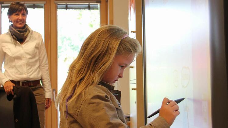 Sabine kringelt am Whiteboard ihren Namen ein. Im Hintergrund ist ihre Lehrerin Beate Schneider zu sehen. Foto: Corinna Igler
