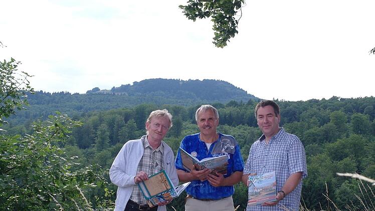 Der Kleine Auersberg im Hintergrund, wo von 1557 bis 1938 Rothenrain gelegen hatte. Über das abgesiedelte Dorf hat Walter Kömpel (Mitte) eine Chronik geschrieben. Unterstützt wurde er von Co-Autor Matthias Elm (rechts) und Layouter Karl Hahn.  Foto: Stephanie Elm