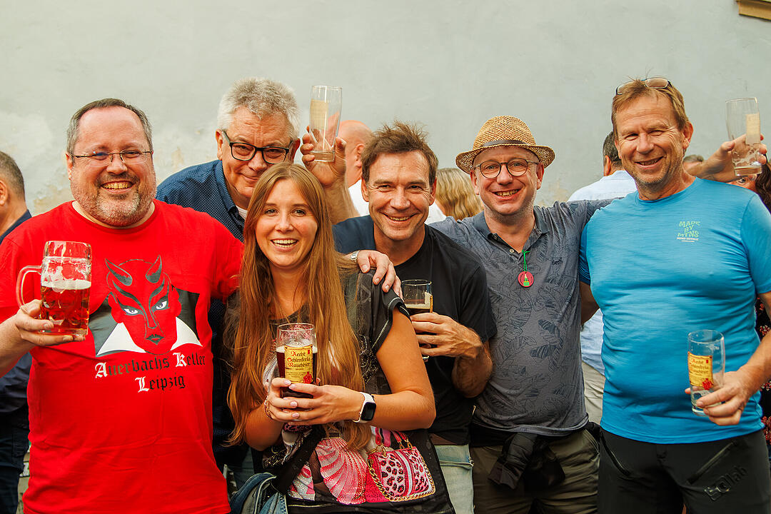 Eine fr&ouml;hliche Gruppe von Menschen h&auml;lt Bierkr&uuml;ge und Sektgl&auml;ser w&auml;hrend der Bamberger Sandkerwa. Feierliche Stimmung und L&auml;cheln in einem geselligen Moment.