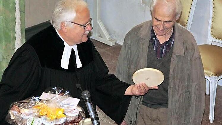 Pfarrer Albrecht Bischoff übergibt ein Geschenk als Dankeschön an den seit 55 Jahren im Ehrenamt wirkendenen Tippach-Hüttenwart Heinrich Zschach.  Foto: Simone Büttner