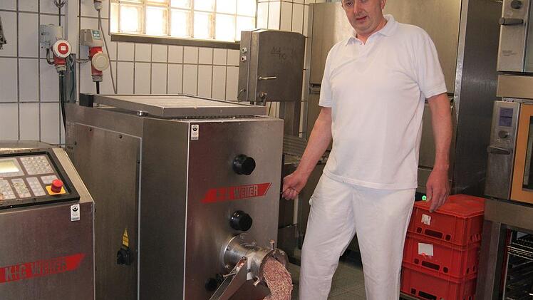 Metzger Spindler betätigt den Fleischwolf.
