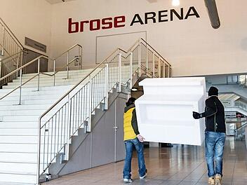 Zwei Männer tragen eine Empfangstheke in die Brose-Arena. Im Foyer wird ein Corona-Impfzentrum aufgebaut.  Foto: Nicolas Armer/dpa