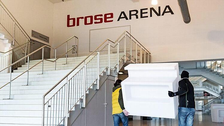 Zwei Männer tragen eine Empfangstheke in die Brose-Arena. Im Foyer wird ein Corona-Impfzentrum aufgebaut.  Foto: Nicolas Armer/dpa