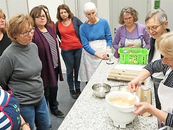 Interessiert schauen die Frauen zu, wie der Brötchenteig löffelweise auf die Backform kommt (rechts: Waltraud Hartmann). Foto: Monika Schütz