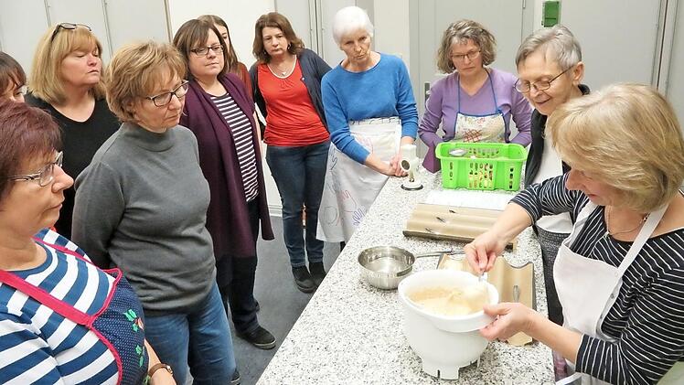 Interessiert schauen die Frauen zu, wie der Brötchenteig löffelweise auf die Backform kommt (rechts: Waltraud Hartmann). Foto: Monika Schütz