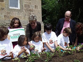 Maria Reinwand erklärt Lilo, wie sie das Salatpflänzchen einsetzen muss. Von links: Selina, Leyel, Melissa, Lilo, Maria Reinwand, Joshua, Samuel, Bürgermeister Thomas Stadelmann, Darleen. Foto: Brigitte Krause