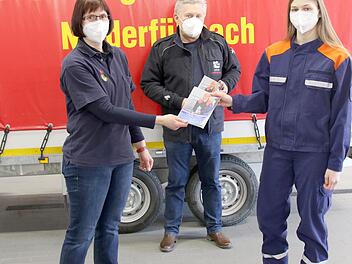 Die Vorsitzende des Kreisjugendfeuerwehrverbandes, Nicole Boßecker (links), übergibt das erste Rätselheft an Luisa Boßecker; dahinter Kreisbrandrat Manfred Lorenz.