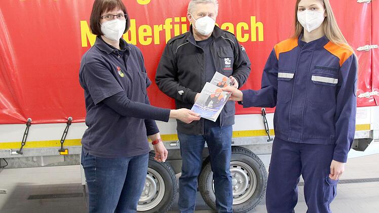 Die Vorsitzende des Kreisjugendfeuerwehrverbandes, Nicole Boßecker (links), übergibt das erste Rätselheft an Luisa Boßecker; dahinter Kreisbrandrat Manfred Lorenz.