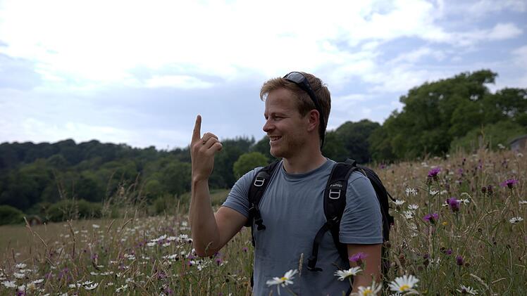Bertie Gregory in einem Wildblumenfeld, mit einer seiner Protagonistinnen auf der Hand.