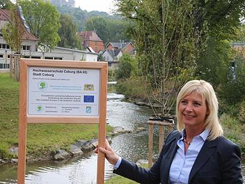 Frau vor Bachlandschaft: Bayerns Umweltministerin Ulrike Scharf vor dem neuen Zusammenfluss von Rottenbach und Lauter. Die Tafel informiert darüber, was dieser Abschnitt des Hochwasserschutzes gekostet hat. Foto: Simone Bastian