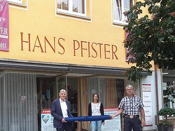 Nicht mit dem symbolischen Schlüssel, sondern zur Branche passend mit einer Stoffrolle übergab Jürgen Pfister (links) seinen Bad Brückenauer Geschäftsbetrieb an Jürgen Bergander (rechts). Ansprechpartnerin vor Ort in der Ludwigstrasse ist für die Kunden weiterhin die Raumausstatterin Martina Arnold (Bildmitte).Foto: Rolf Pralle