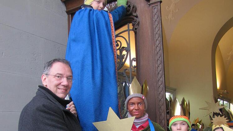 Bürgermeister Thomas Nowak lässt sich den Segen von Caspar, Melchior und Balthasar an der Rathaustüre bestätigen. Rufus steht auf der Leiter, Jetta gleich daneben. Damit nichts passiert, hält Thomas Nowak die Leiter fest. Foto: Martin Koch