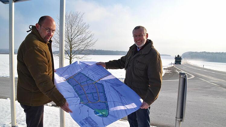 Bürgermeister Waldemar Bug (rechts) und Planer Johannes Hahn stehen hier an der Abfahrt von der Bundesstraße 286 zur Kreisstraße 15 und halten einen ersten Plan für das neue Gewerbegebiet in ihren Händen. Das soll auf der Fläche links der Bundesstraße Richtung Poppenroth entstehen. Foto: Kathrin Kupka-Hahn