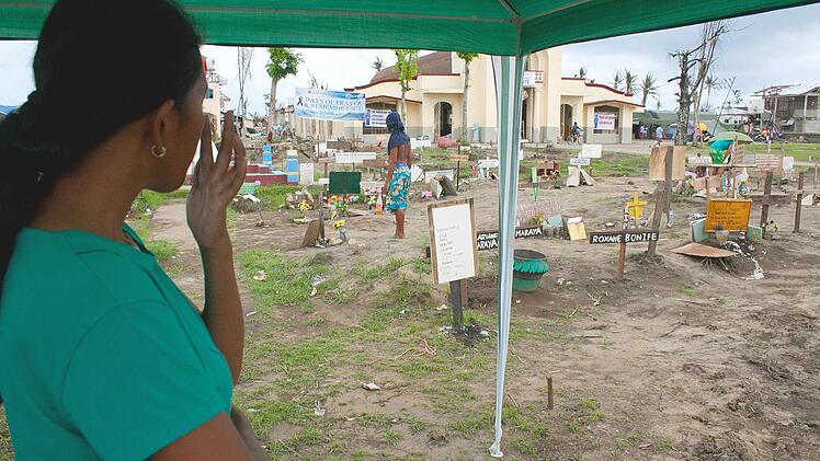 Die 22-jährige Michelle Maraya blickt vor der katholischen Kirche von San Joaquin auf den Philippinen auf Massengräber, in denen Opfer des Taifuns "Haiyan" beerdigt wurden. Foto: John Grafilo/dpa