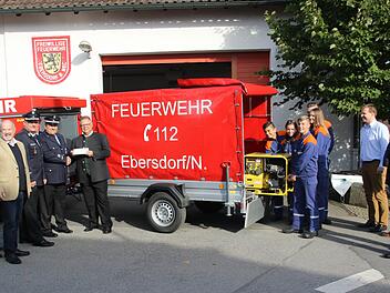 Kommandant Norbert Engel übergibt den Anhänger an den Dritten Bürgermeister der Stadt Neustadt, Martin Stingl. Währenddessen hebt  die Feuerwehrjugend aus Ebersdorf bei Neustadt schon einmal das Stromaggregat aus dem Anhänger. Foto: Michael Stelzner