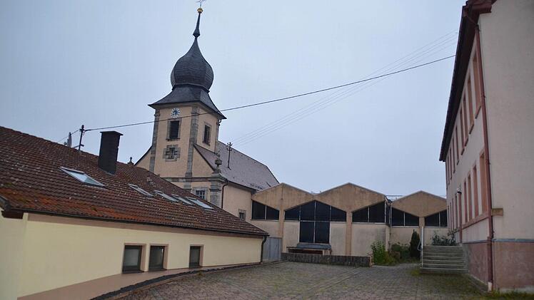 Die Gebäude an der Kirche stehen nah beieinander: Rechts ist die alte Schule zu sehen, links das ehemalige Lebensmittelgeschäft. Letzteres wird für den Umbau der Kirche weichen, ebenso wie der Anbau St. Pius in der Bildmitte. Auch der Schulhof wird verändert, denn die Mauer zur Kirche soll ebenfalls abgerissen werden. Foto: Kathrin Kupka-Hahn