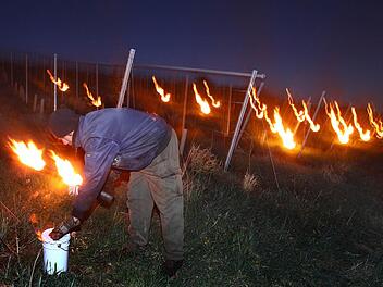 Kellermeister Johannes Weickert entzündet am 16.04.2014 kurz vor Sonnenaufgang in den Weinbergen bei Bimbach (Bayern) mit Paraffin betriebene Frostkerzen um die Reben vor der Kälte zu schützen. Foto: Karl-Josef Hildenbrand/dpa