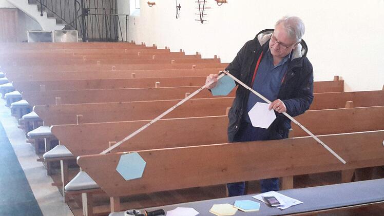 In Krisenzeiten wird selbst ein Pfarrer zum Handwerker. Gerd Kirchner fixiert an den Sitzbänken des Gotteshauses gut sichtbare Markierungspunkte, damit die Besucher der Bad Brückenauer Friedenskirche ausreichend Abstand voneinander halten.Foto: Rolf Pralle