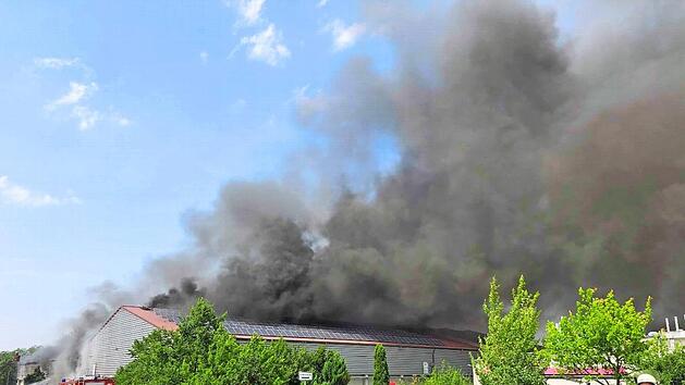 Dicke Qualmwolken dringen aus der Halle des Entsorgungsbetriebes. Der Wind treibt sie &uuml;ber das Gel&auml;nde des Unternehmens und &uuml;ber das Areal einer benachbarten B&auml;ckerei davon. Am Montag war das Feuer kurz vor 15 Uhr ausgebrochen. Der Rauch beeintr&auml;chtigte auch den Verkehr auf den umliegenden Stra&szlig;en. Foto: News5/Ferdinand Merzbach