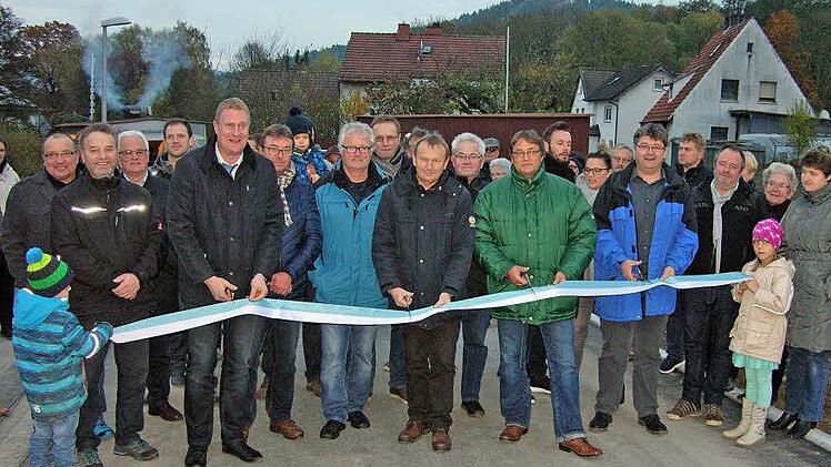 Bürgermeister Michael Keilich, Vertreter der Gemeinde und der an der Erschließung beteiligten Firmen schneiden im Beisein künftiger Bauherren und etlicher Gäste das Band durch. Foto: Klaus Oelzner