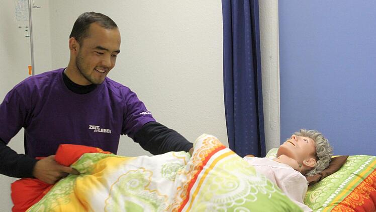 Ali Sharifi deckt im Proberaum der Altepflegeschule eine Puppe zu - während seine Klassenkameraden bereits praktisch in Altenheimen arbeiten. Wegen einer Formalität darf Sharifi seine Ausbildung derzeit nicht weiterführen. Ob er überhaupt bleiben kann, ist ungewiss. Foto: Markus Klein