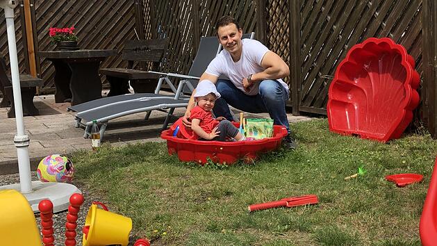 Der ganze Stolz heißt Clara. Während Georg Eckstein im heimischen Garten über das ganze Gesicht strahlt, schaut seine kleine Tochter doch eher skeptisch aus der roten Sandkastenschüssel. Wird de Papa wirklich Arzt in Neustadt...? Foto: Christoph Böger