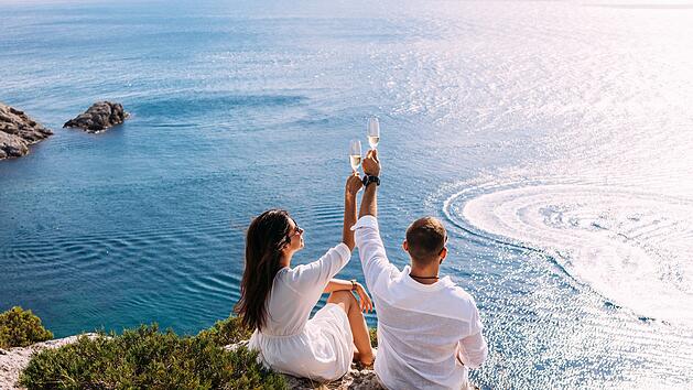 Luxus-Urlaub - all inclusive Ein verliebtes Paar feiert seine Verlobung am Meer. Ein sch&ouml;nes Paar trinkt Champagner am Meer. Flitterwochenreise. Verliebte am Strand. Hochzeitsreise. Paar im Urlaub. Freiraum. A couple in love celebrates their engagement on the seashore. A beautiful couple drinks champagne by the sea. Honeymoon trip. Lovers on the beach. Wedding travel. Couple on vacation. Copy space