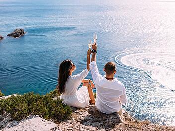 Luxus-Urlaub - all inclusive Ein verliebtes Paar feiert seine Verlobung am Meer. Ein sch&ouml;nes Paar trinkt Champagner am Meer. Flitterwochenreise. Verliebte am Strand. Hochzeitsreise. Paar im Urlaub. Freiraum. A couple in love celebrates their engagement on the seashore. A beautiful couple drinks champagne by the sea. Honeymoon trip. Lovers on the beach. Wedding travel. Couple on vacation. Copy space