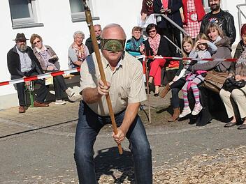 Altbürgermeister Günther Kob wurde ausgelost und musste als Hahnenschläger in den Ring. Edgar Rödel und Tobias Baum verbanden dem Bürgermeister die Augen und gaben ihm den Dreschflegel in die Hand. Foto: Michael Stelzner