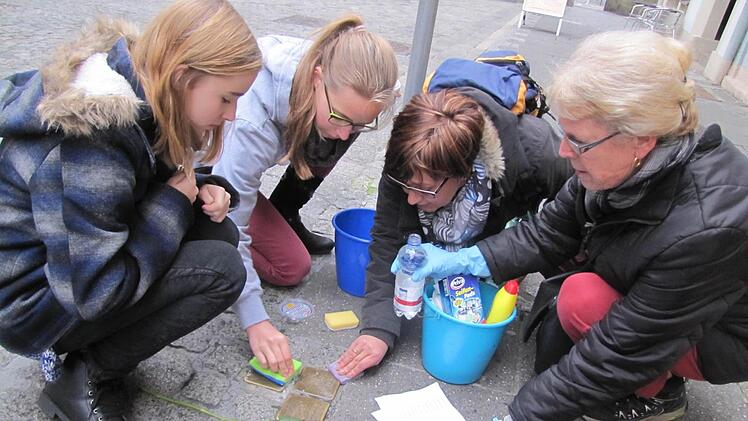 Victoria Renger, Jasmin Parys, Maria del Carmen Schmucker-Brabec und Hanne Plentz (von links) schrubben in der Judengasse die Stolpersteine von Hermann Wolf und Frieda Baumwollspinner, die einst dort gewohnt hatten. Foto: Martin Koch