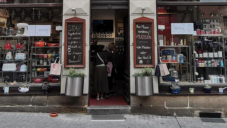 Ein traditionsreiches Geschäft in der Bamberger Altstadt schließt bald. Schaufenster mit Küchenartikeln und Schildern, die auf Verkaufsangebote hinweisen. Kunden betreten den Laden.