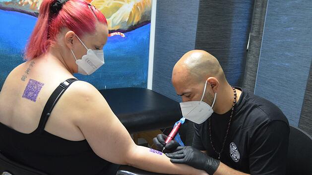 Der Code als Impfnachweis hat sich auch vergr&ouml;&szlig;ert (auf dem R&uuml;cken) nicht lesen lassen. Stephanie Hornung l&auml;sst sich von Tattoo-K&uuml;nstler Navid einen anderen Code stechen, der sie an die Corona-Zeit erinnern soll - es ist der von Navids Tattoo-Studio "Villa Bunter Hund".