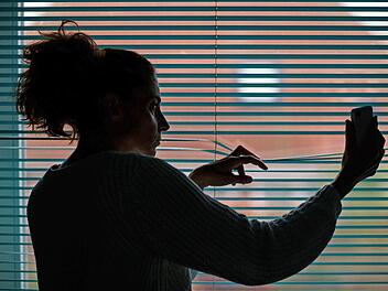 Eine Frau beobachtet auf diesem Symbolfoto durch eine Jalousie nach einem Stalking-Anruf die Straße vor ihrer Wohnung.  Foto: Jens Büttner, dpa