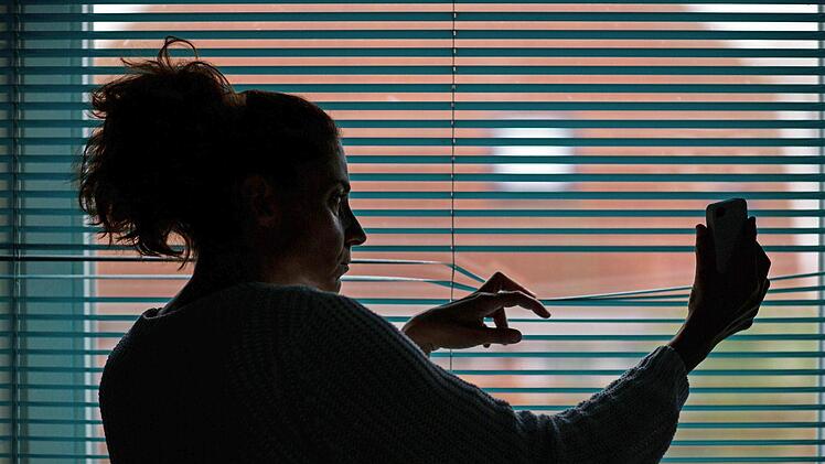 Eine Frau beobachtet auf diesem Symbolfoto durch eine Jalousie nach einem Stalking-Anruf die Straße vor ihrer Wohnung.  Foto: Jens Büttner, dpa