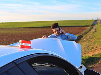 Neue Regel für Autofahrer in Spanien: Verpflichtende V16-Warnleuchte ab 2026 Ab dem 1. Januar 2026 modernisiert Spanien die Sicherheitsvorkehrungen im Straßenverkehr. Das traditionelle Warndreieck hat ausgedient und wird durch die innovative V16-Warnleuchte ersetzt. Kaukasischer Mann telefoniert und schaut auf den Motor mit der Notfallleuchte V16, tagsüber. Konzept eines Problems auf der Straße von Sergio Caucasian man calling on the phone looking at the engine with the emergency light V16, daytime. Concept of problem on road