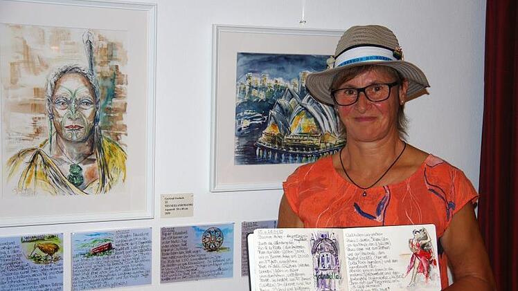 Gertrud Gerlach stellt aktuell 20 Aquarelle im Golfclub aus. Das Foto zeigt im Hintergrund eine Abbildung des Opernhauses von Sydney und das Bildnis eines Maori-Häuptlings, in der Hand hält sie ihr Skizzen-Tagebuch.  Fotos: Klaus Werner