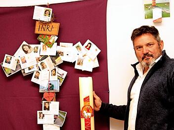Trauerbegleitung: Diakon Joachim Stapf in seinem Arbeitszimmer vor einem Kreuz mit Bildern von Kindern und Personen, die er begleitet hat; daneben steht die Osterkerze. Der Diakon hat seinen Arbeitsplatz in der Pfarreiengemeinschaft "Maintal - Heilige Länder". Foto: Günther Geiling